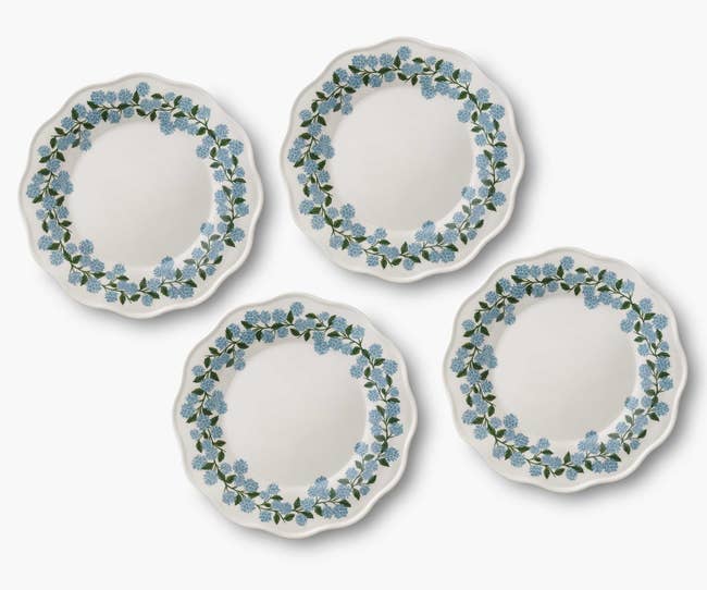 Four decorative plates with floral edge designs featuring blue flowers and green leaves