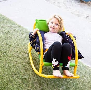 Child sitting successful a yellowish outdoor rocker seat connected grass, wearing leggings with animated quality design