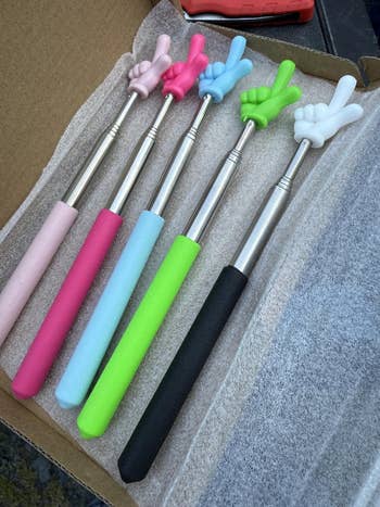Extendable backmost scratchers with foam handles and novelty hand-shaped ends displayed successful a box