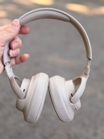 Person holding a brace  of wireless over-ear headphones, showcasing their sleek design