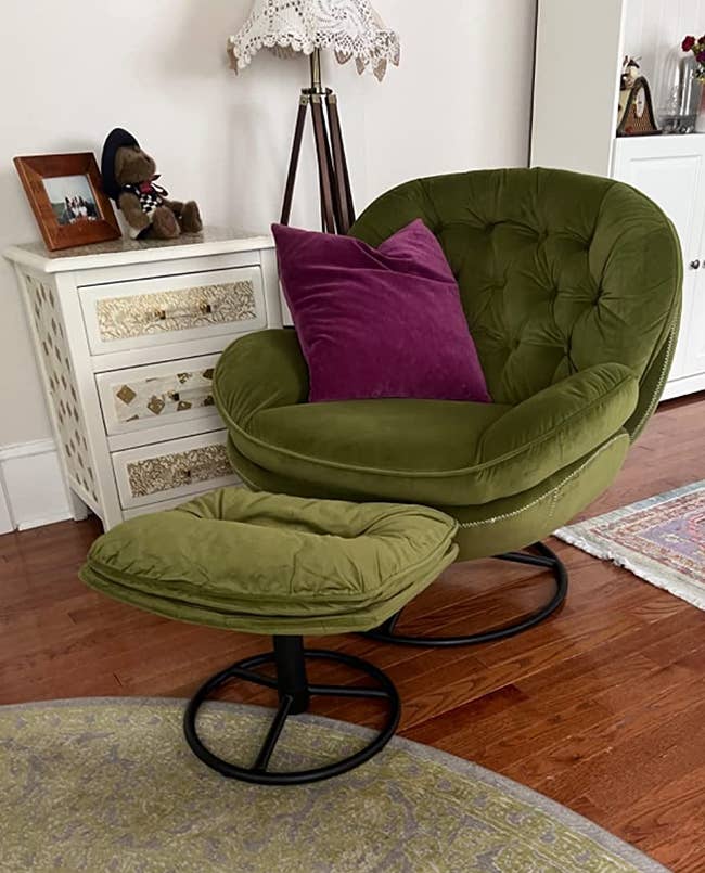 Green wide rounded armchair with small ottoman and black metal circular stand decorated with a purple throw pillow