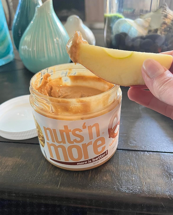 A reviewer dipping an apple in a jar of white chocolate pretzel peanut butter 