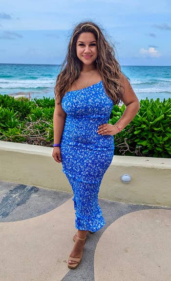 reviewer in a blue floral dress standing on a sidewalk by the beach