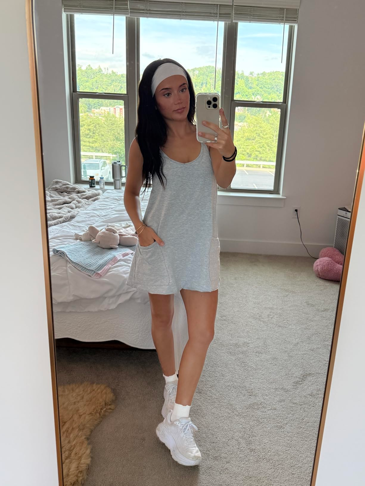 Person successful  a casual sleeveless dress, headband, and sneakers taking a reflector  selfie successful  a chamber  with a neatly made furniture  successful  the background