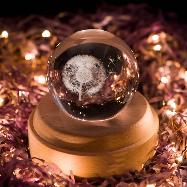 the crystal ball with a dandelion design inside, on a wooden pedestal