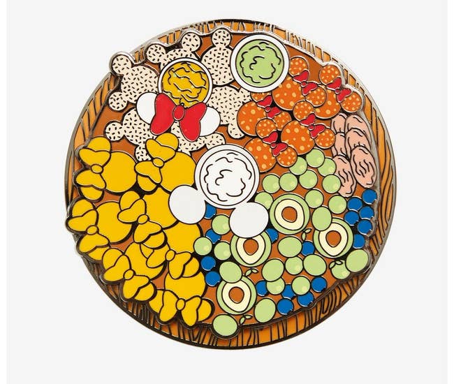 an enamel pin of a Charcuterie board with mickey-shaped items on it