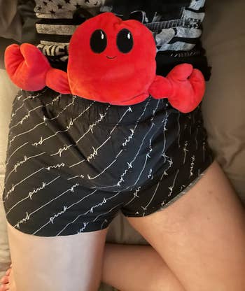 reviewer photo of the red plush lobster heating pad sticking out of their shorts