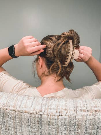 Person utilizing a ample  hairsbreadth  clip to unafraid  their hairsbreadth  into a bun portion    seated