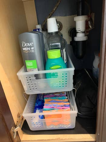 reviewer's clear slide-out baskets under a bathroom cabinet holding various toiletries