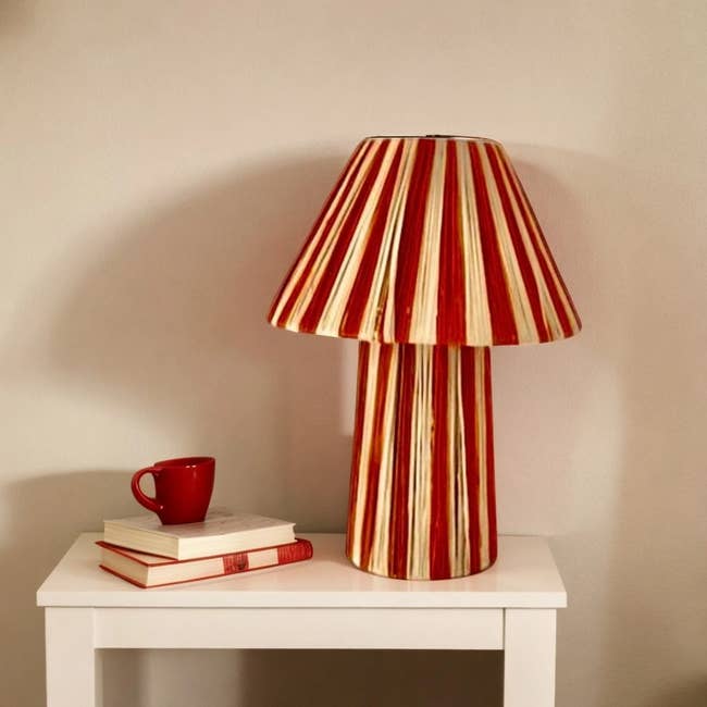 Red and achromatic striped array lamp connected a achromatic table, adjacent to 2 stacked books and a reddish cup