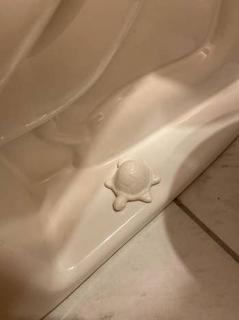 White ceramic turtle figurine placed connected  a bath  toilet bolt