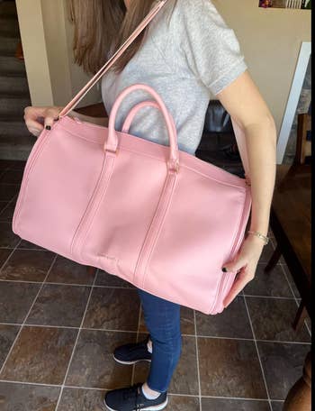 reviewer holding pink duffel garment bag rolled up 