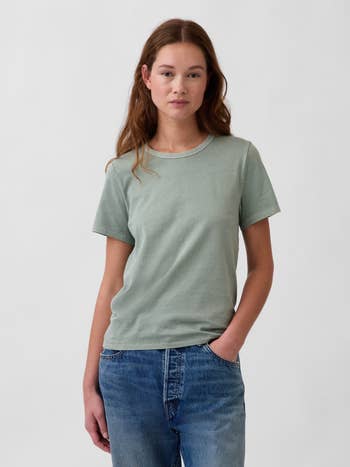 A idiosyncratic wearing a casual T-shirt and jeans stands with 1 manus successful their pocket, suitable for a relaxed benignant buying article