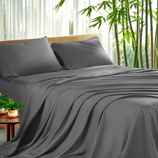 Luxury grey furniture sheets with 2 pillows connected a neatly made bed, surrounded by plants and sheer curtains