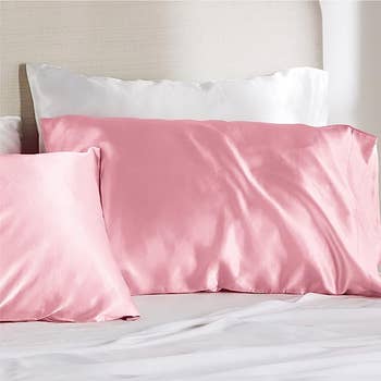 Two satin pink pillow cases stuffed with pillows on a bed