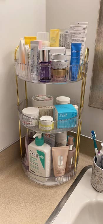 A three-tiered bathroom storage rack filled with various skincare products and toiletries