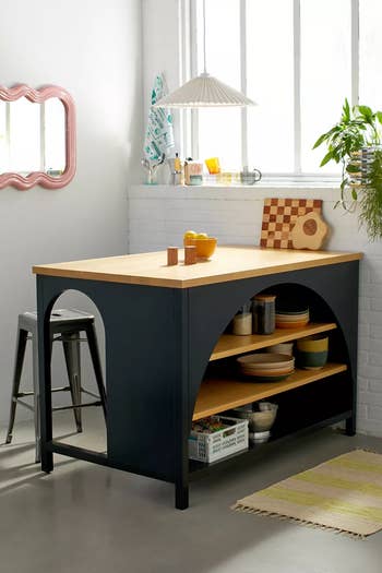 Modern kitchen island with wooden top, open shelving, and mismatched ceramic decor in a bright space with a window