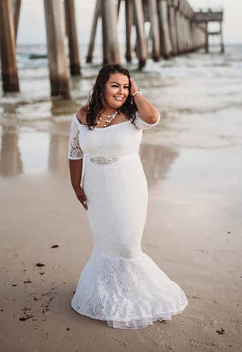 Reviewer wearing white lace mermaid dress with off the shoulder quarter sleeves standing on the beach