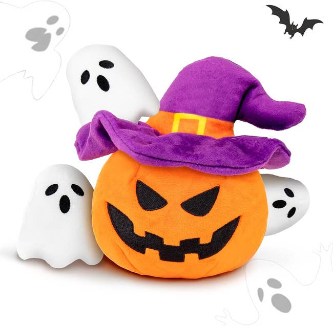 Plush pumpkin wearing a pointed witch hat, surrounded by smiling shade figures. A decorative bat is successful the background