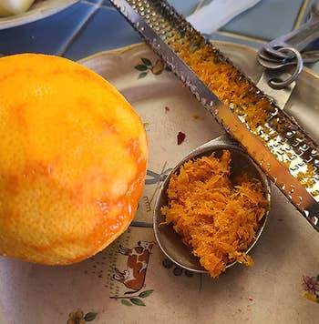 reviewer photo of the microplane next to a tablespoon full of orange zest and a zested orange