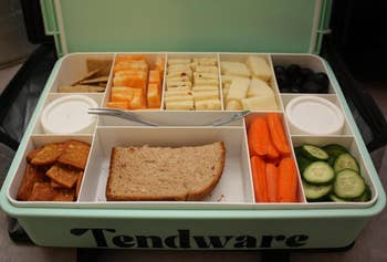 Lunchbox with sandwich, food  slices, crackers, achromatic  olives, carrot sticks, and cucumber slices organized successful  compartments with a fork