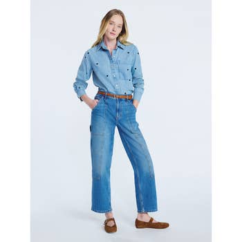 Person poses in relaxed denim shirt and jeans, hands in pockets, wearing brown flats. Casual outfit for a stylish, laid-back look