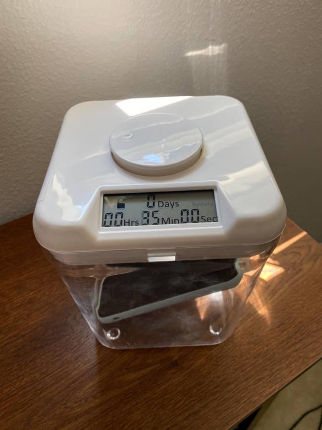Kitchen safe container with a digital timer lock on the lid and a phone inside, displaying time remaining until it unlocks