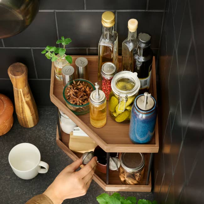 Kitchen corner shelf organizer with spices, oils, and jars. A person's hand reaches for a container, showcasing organized storage solutions