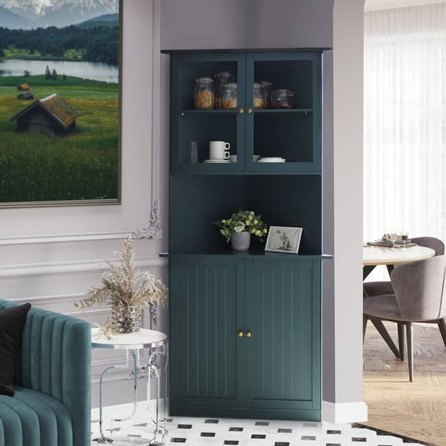 a tall teal corner cabinet with glass cabinets on top and solid closed cabinets on the bottom