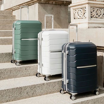 three differently colored Freeform suitcases on steps