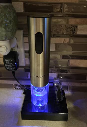 reviewer's wine opener with glowing blue light on its charging stand, foil cutting tool is next to it