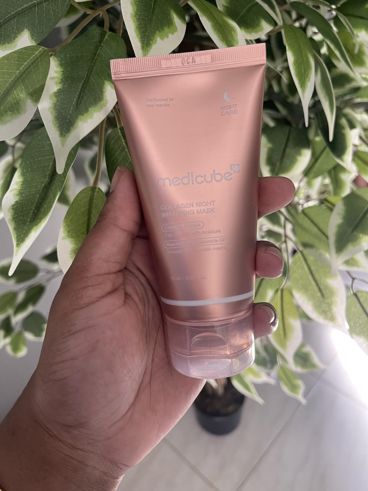 Person holding Medicube Collagen Night Wrapping Mask successful  beforehand   of a leafy plant. Product is simply a skincare item