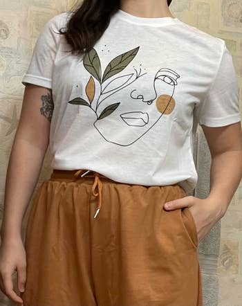 reviewer wears a white t-shirt with a drawn portrait on it
