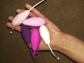 A reviewer's hand holding five differently-shaped and sized Kegel exercise weights