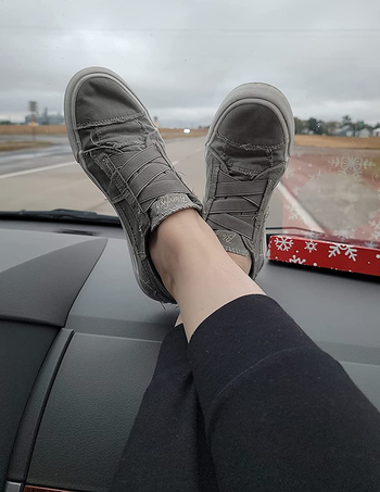 reviewer wearing the grey sneakers with feet up on car dashboard