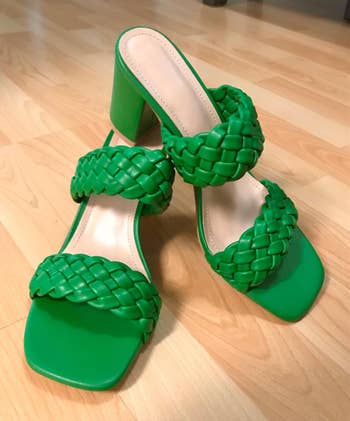 A pair of green braided high-heel sandals on a wooden floor