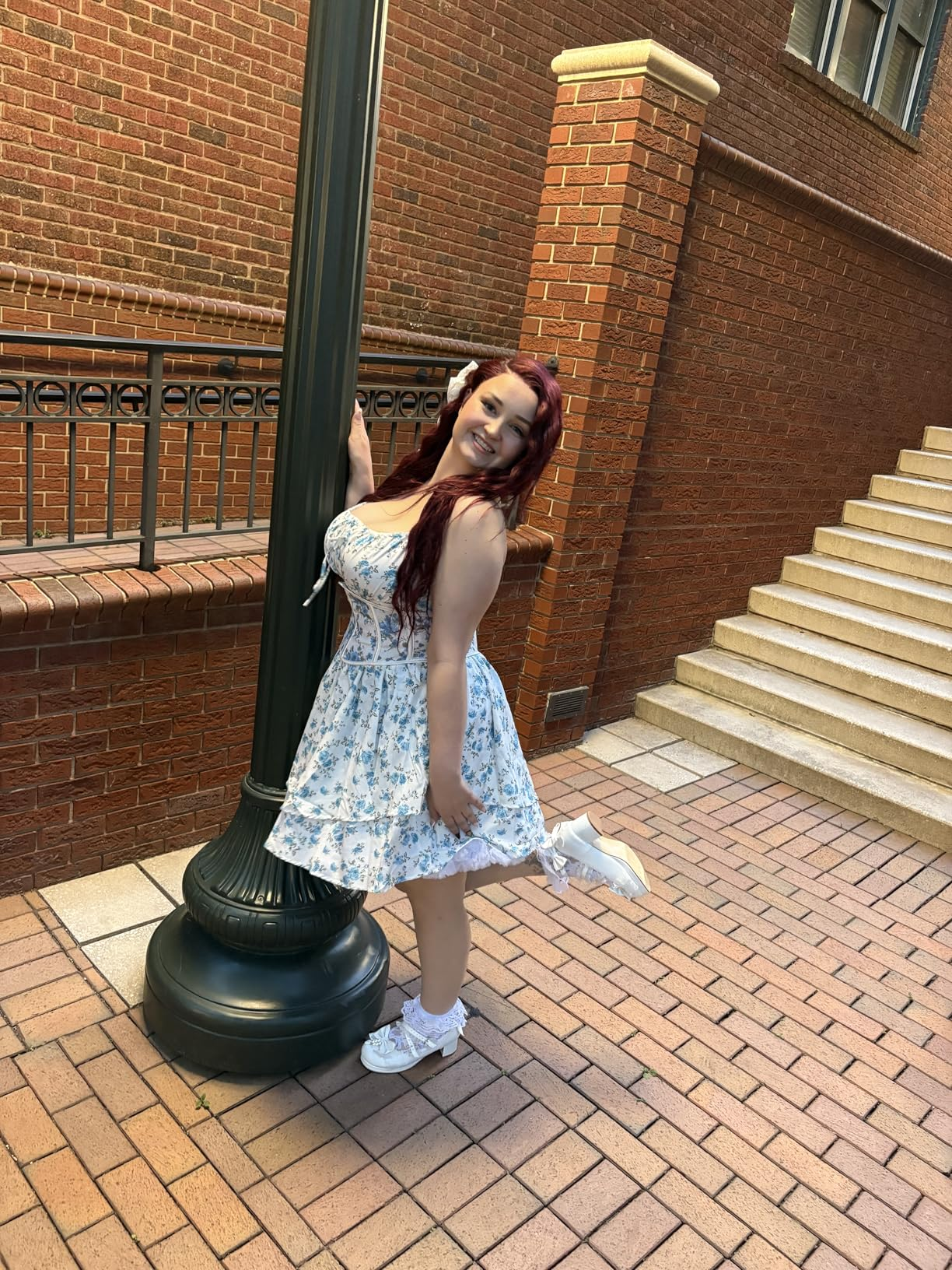 Person successful  a floral formal  poses adjacent  to a lamppost connected  a ceramic  pathway, smiling with 1  ft  raised