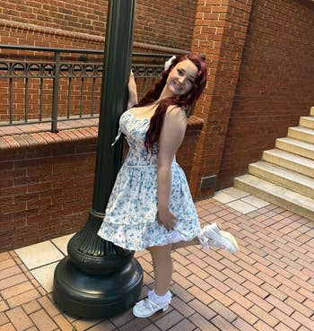 Person successful a floral formal poses adjacent to a lamppost connected a ceramic pathway, smiling with 1 ft raised