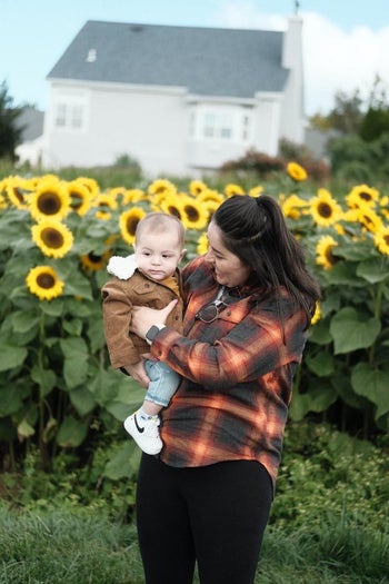 buzzfeed editor wearing an orange and black flannel holding a baby in front of sunflowers