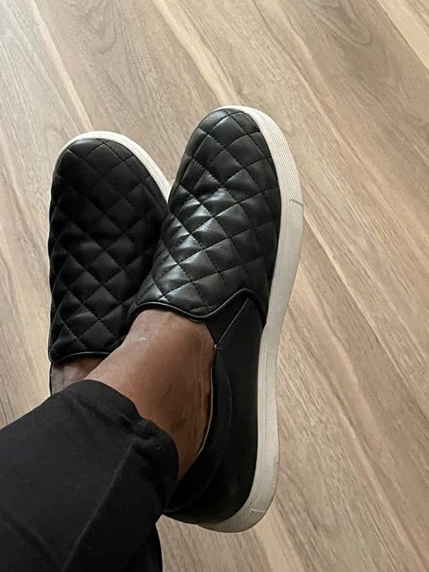 Quilted slip-on sneakers worn with black pants, shown from above, on a light wood floor