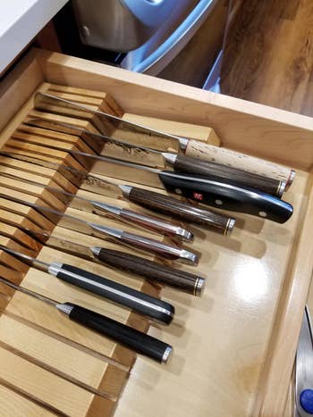 A drawer with organized, assorted kitchen knives in a wooden organizer, showcasing a variety of handle designs
