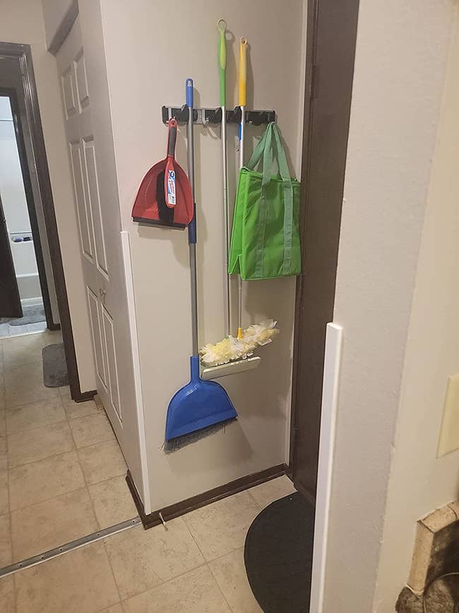 The organizer installed on a wall holding a duster, broom, and shopping bag