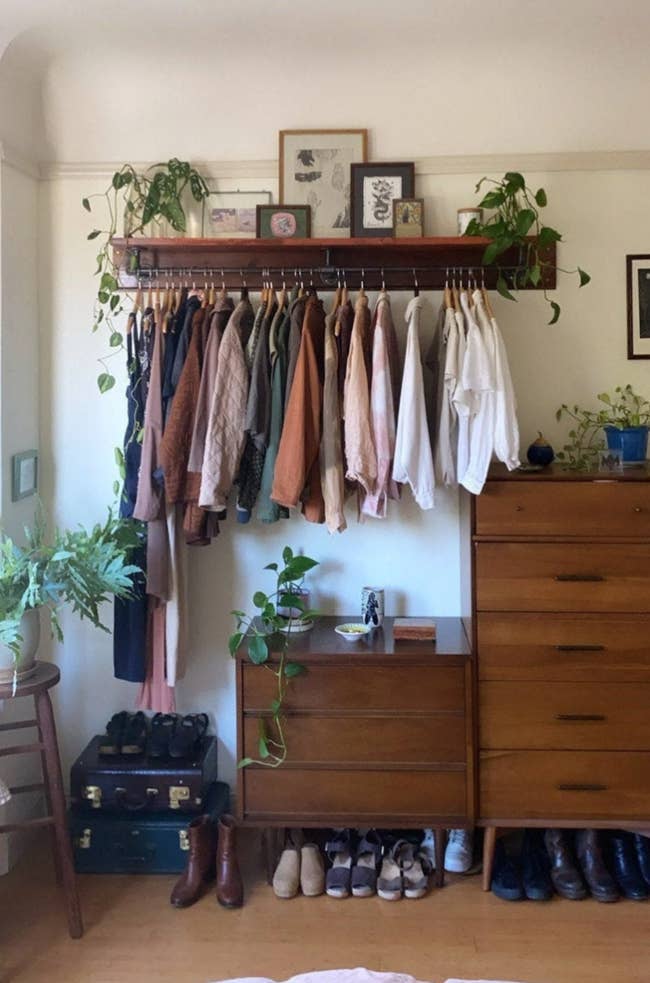 the long metal rack with clothes hanging from it and a shelf with art on top
