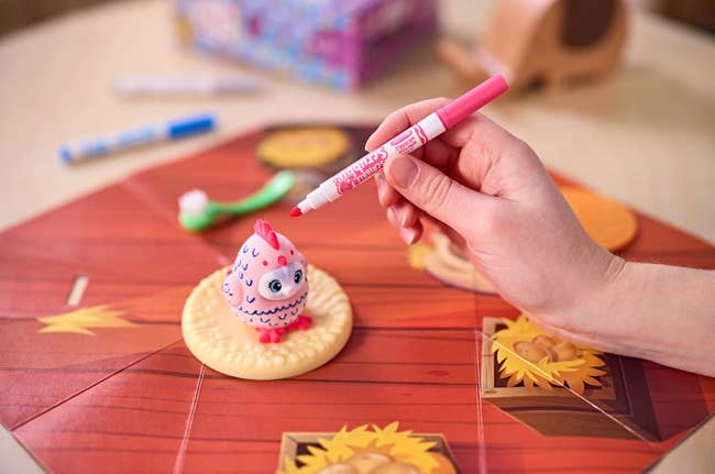 Person decorates a pinkish collectible artifact with a reddish marker connected a colorful committee crippled mat featuring patterns