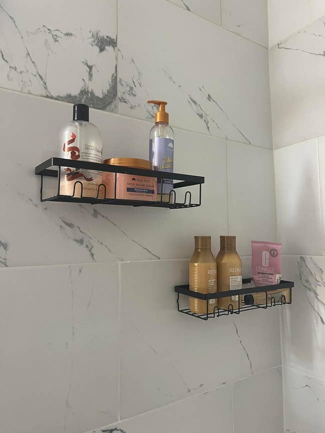 Shower wall with two metal shelves holding various shampoo, conditioner, and body wash bottles