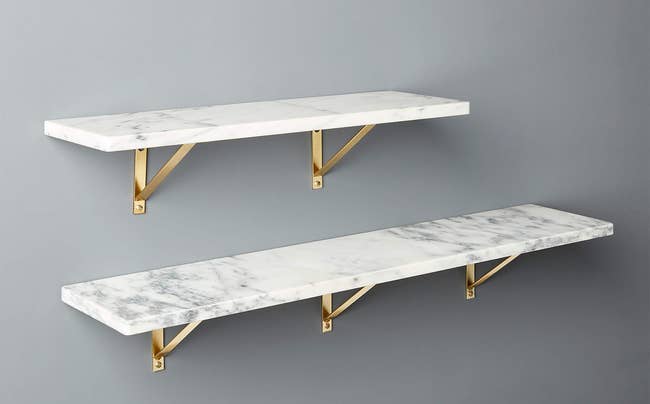Two marble wall-mounted shelves with gold mounting supplies on a gray wall