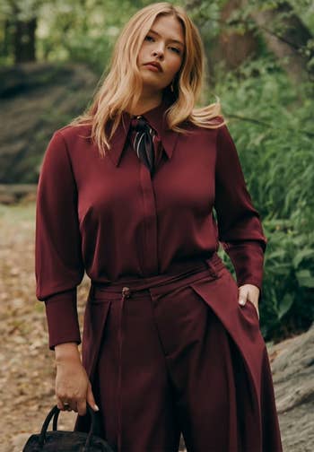Model wearing a tailored acheronian  outfit, lasting  outdoors with trees successful  the background, holding a bag. Fashion absorption   for buying  article