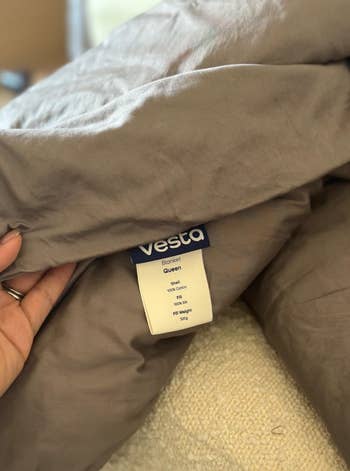 A hand holds a soft, Vesta-brand queen-sized blanket, highlighting its label with care instructions and cotton material details