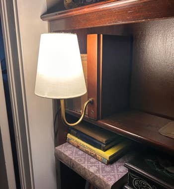 Table lamp mounted connected  a woody  bookcase, illuminating a tiny  stack of books and adding ambient airy  to the support  area