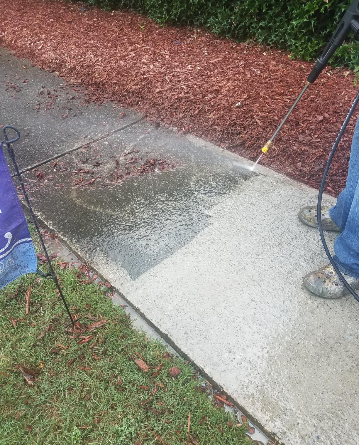 a sidewalk being pressure washed, showing a super grimy dirty side and a side that's already been cleaned and looking noticeably much better